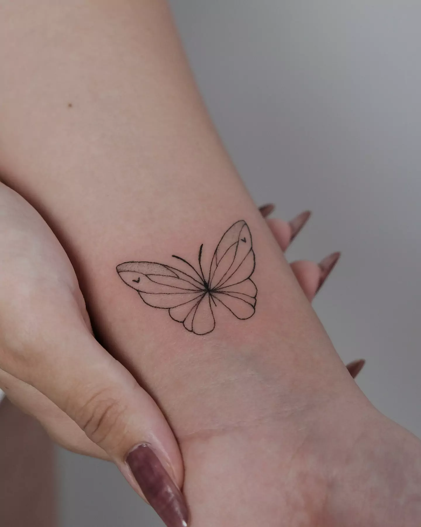 simple black outline butterfly tattoo on wrist